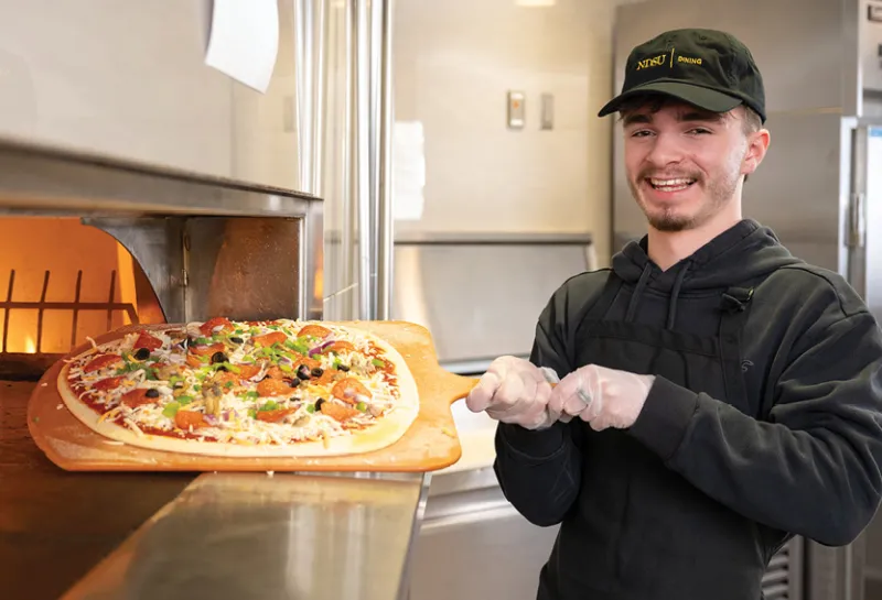 Dining worker holding a pizza about to go in the oven