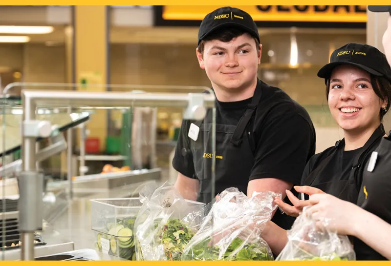 Students smiling and working at the salad bar
