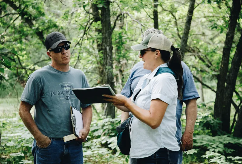 A woman in a baseball cap discusses a plan with two gentlemen
