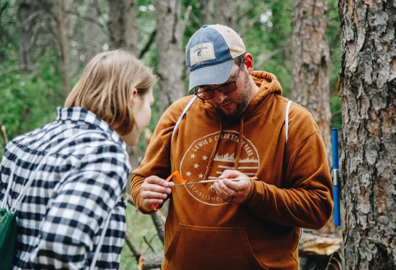 A man in a baseball cap and a woman look at a core of a tree