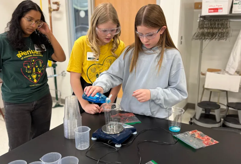 two young girls mixing liquid soap into a beaker at STEM event