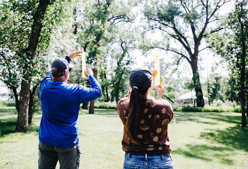 Two educators use a ruler to measure the height of a tree