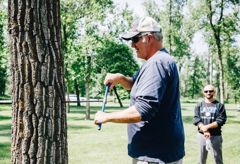 A man uses an increment borer to take a core sample from a tree