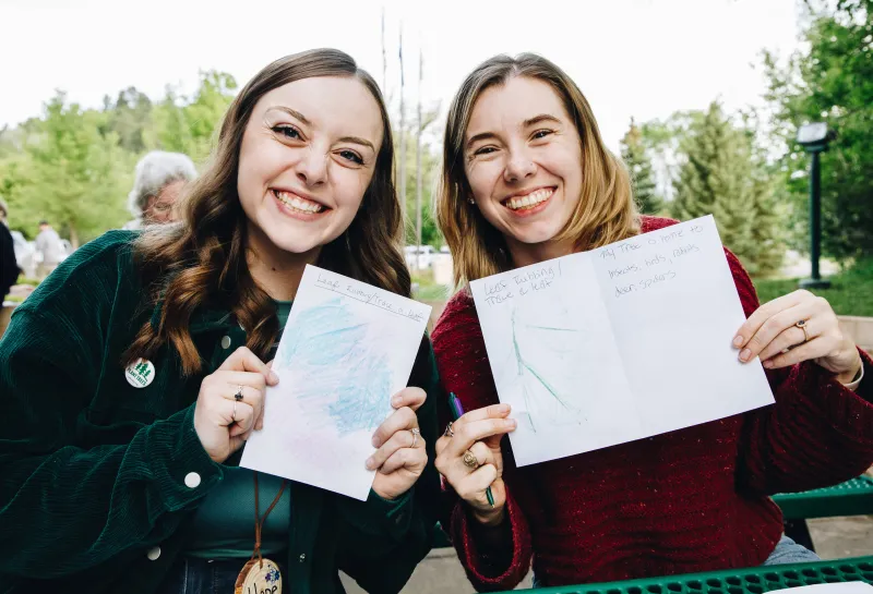 Two women smile holding up a drawing of leaves