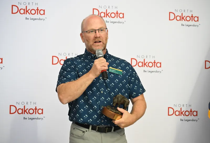 A man in glasses gives a speech while holding a bison-shaped award
