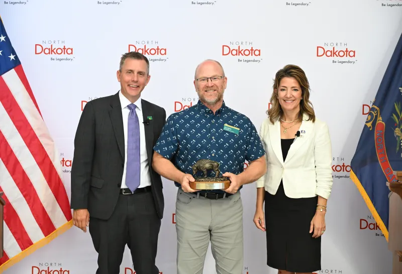 A man holds a bison-shaped award next to a man and woman