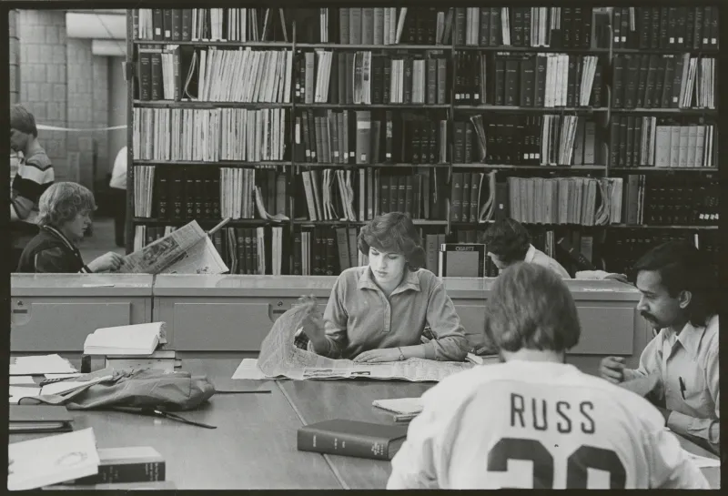 Students sit around a table in NDSU's Main Library to look through books and newspapers.