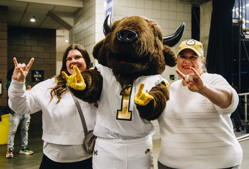 Two women throw the bison horn hand sign up with a bison mascot