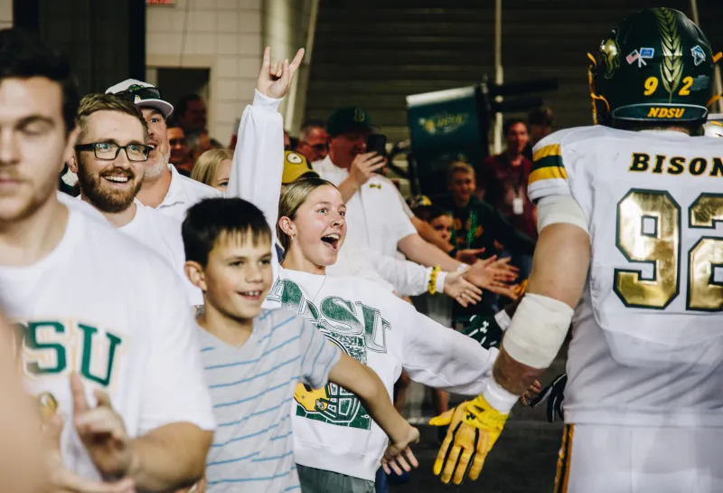 A girl throws the bison horns hand sign up as she high fives a football player