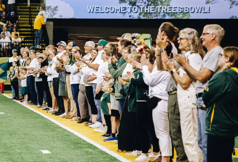 A line of people clap as they are recognized on a football field