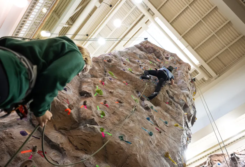 male student climbing rock wall with female student acting as belay