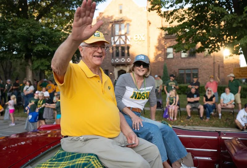 Robert and Sheila Challey wave to the crowd while riding in a car as part of the Homecoming 2025 parade