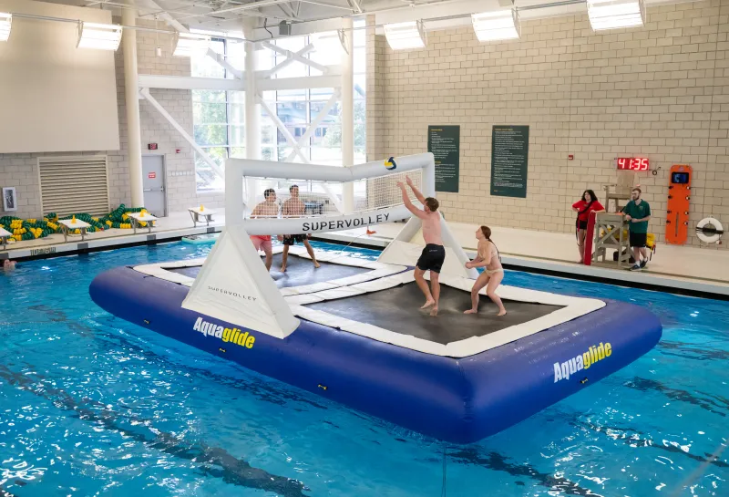 male students playing volleyball on an inflatable trampoline in a pool
