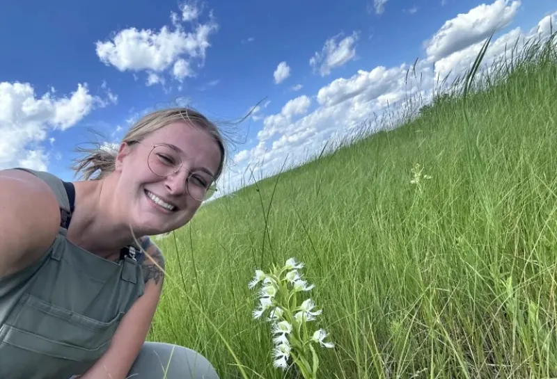 Trinity Atkins smiling at camera will sitting in a green grassy field. 