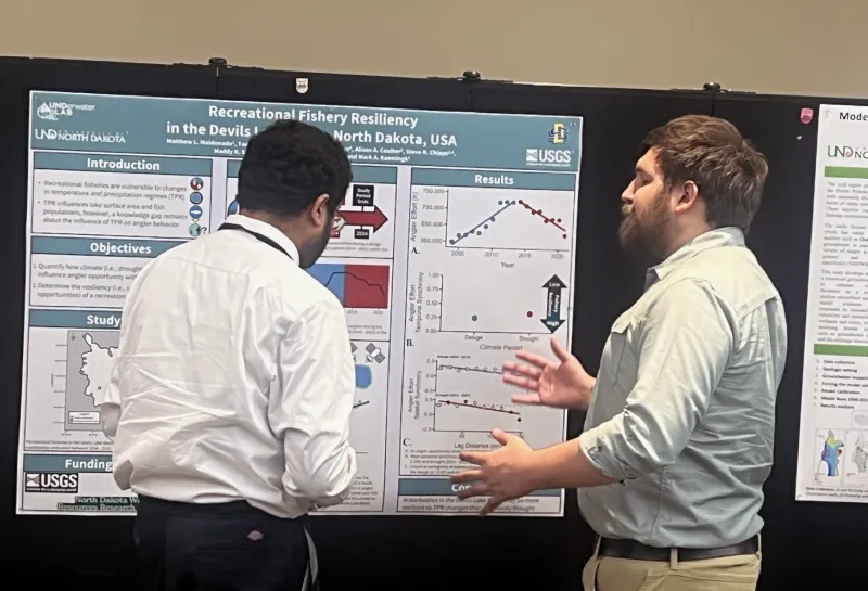 Two men discussing a scientific research poster titled "Recreational Fishery Resiliency in the Devils Lake Basin, North Dakota, USA."