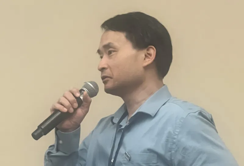 NDSU associate professor and NDWRRI interim director Trung Le wearing a light blue button-up shirt and a conference badge, holds a microphone as he speaks.
