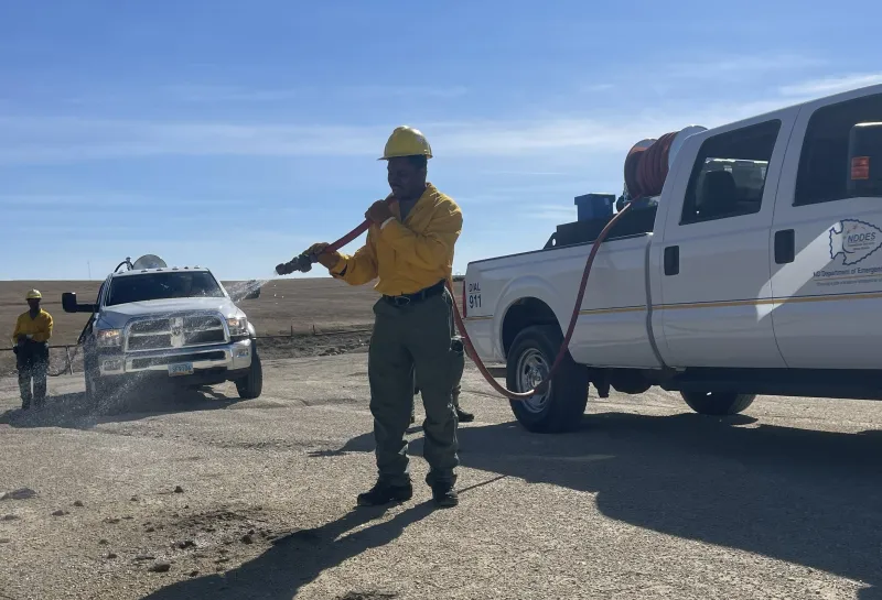 A wildland firefighter uses a hose and truck to prepare to fight fires.