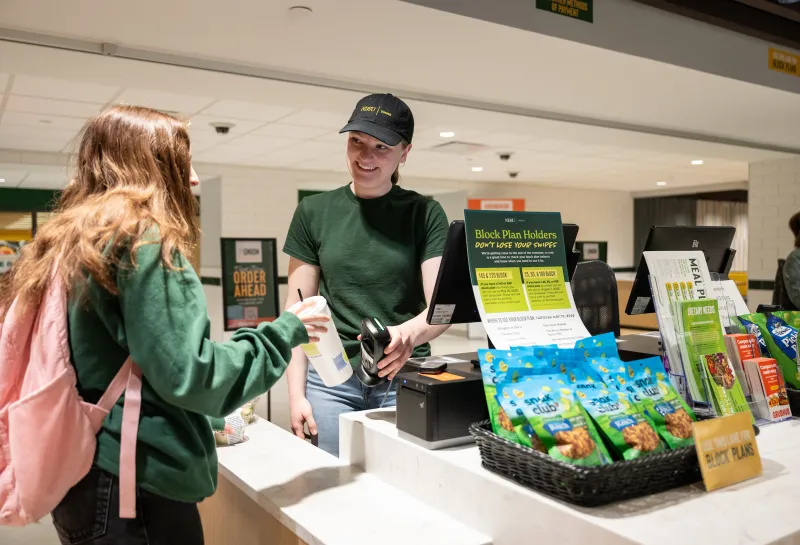 student working in the union market checking out another student at the checkout counter