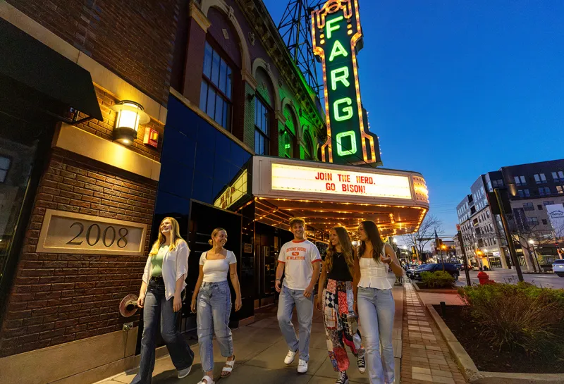 NDSU students walking under the Fargo Theatre sign at night