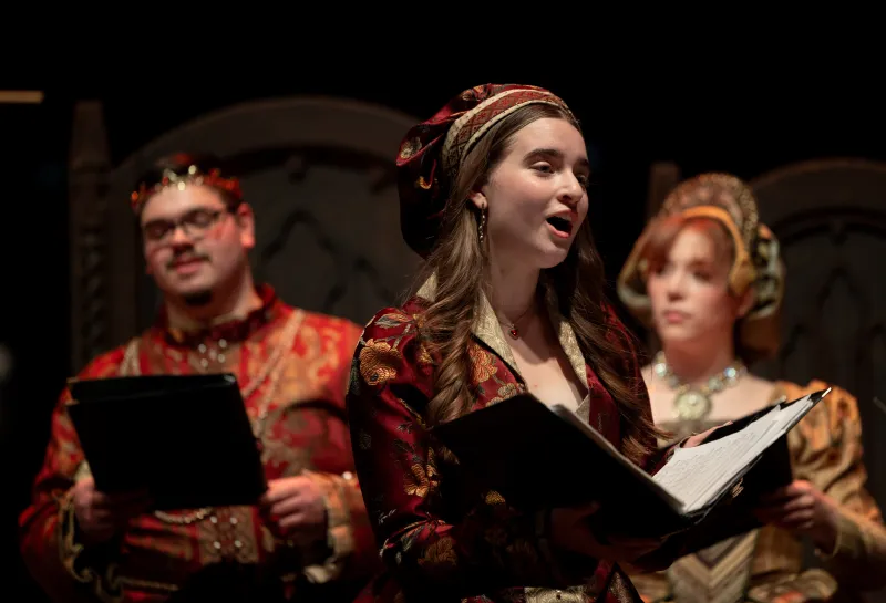 A female NDSU student singing in the Madrigal Dinners while dressed in Renaissance regalia.