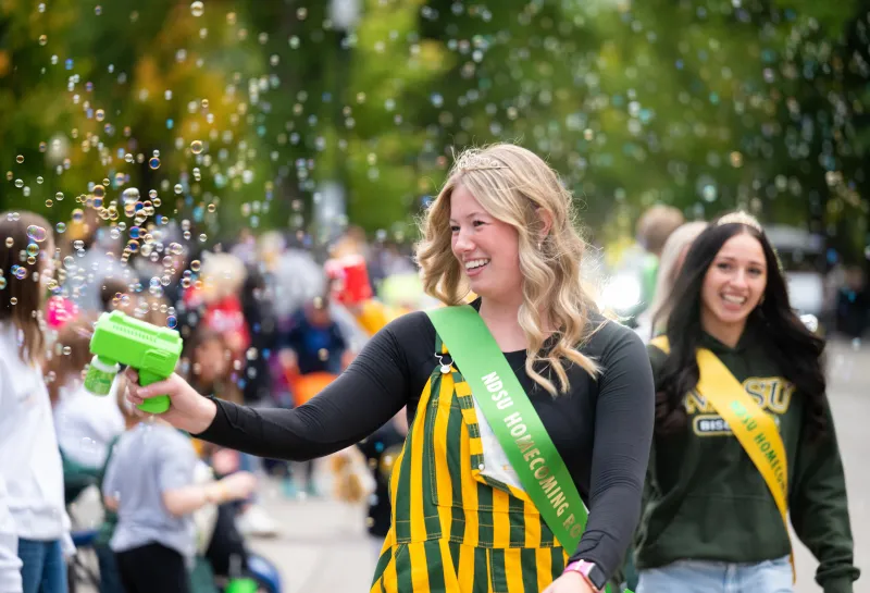 a member of the Homecoming Court playfully blows bubbles at spectators during the Homecoming parade