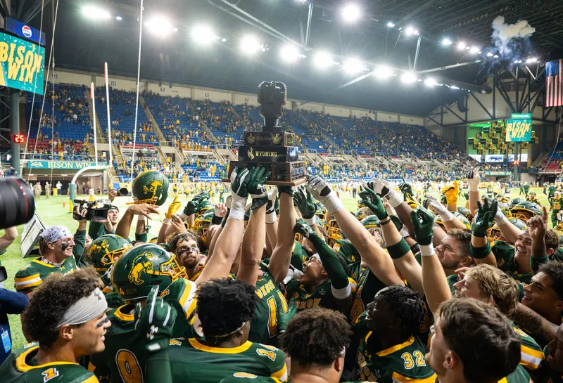 Bison football team celebrate their Homecoming game win by hoisting the trophy