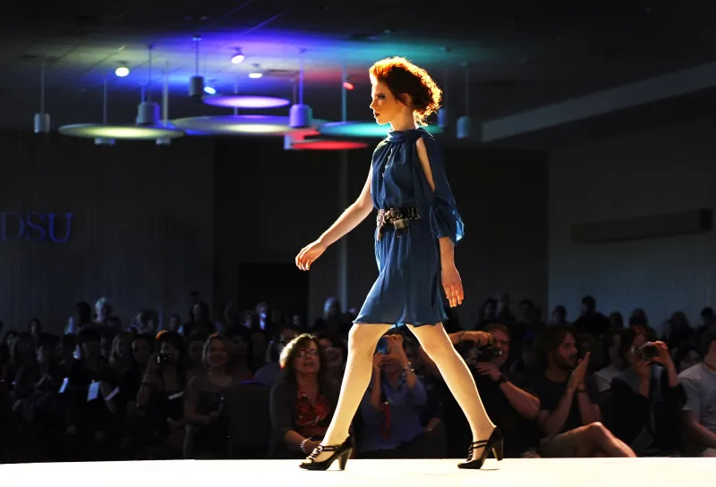 Model wearing a blue dress while walking on runway.