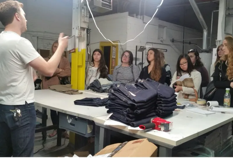 Students listening to a presenter while standing at table with denim.