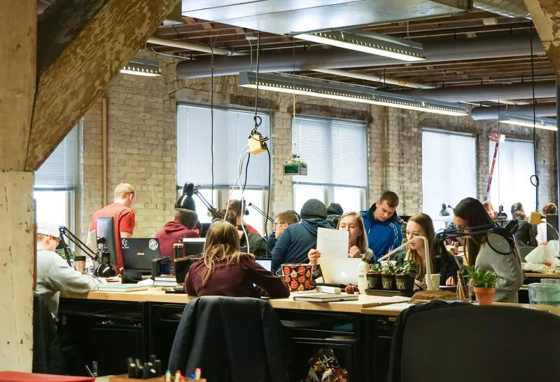 Architecture studio with students working at large tables with computers and other supplies.
