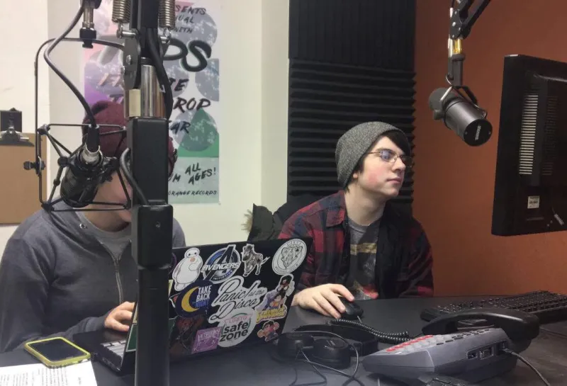 Students in control room with monitors, laptop, microphone and other equipment.