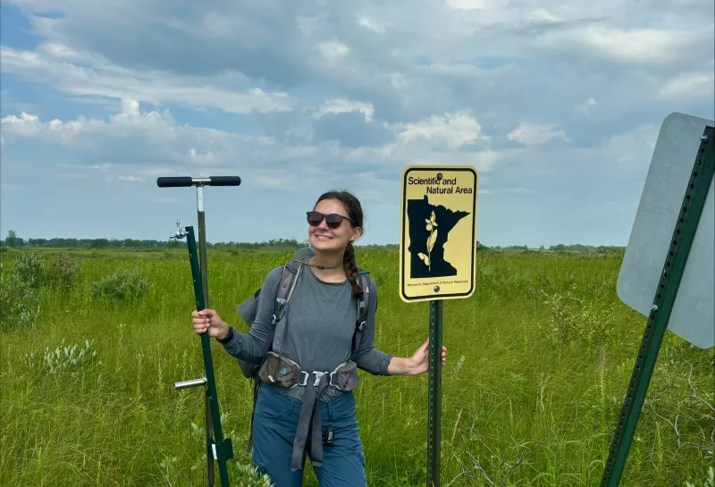 Josie Pickar standing in field holding equipment and sign.