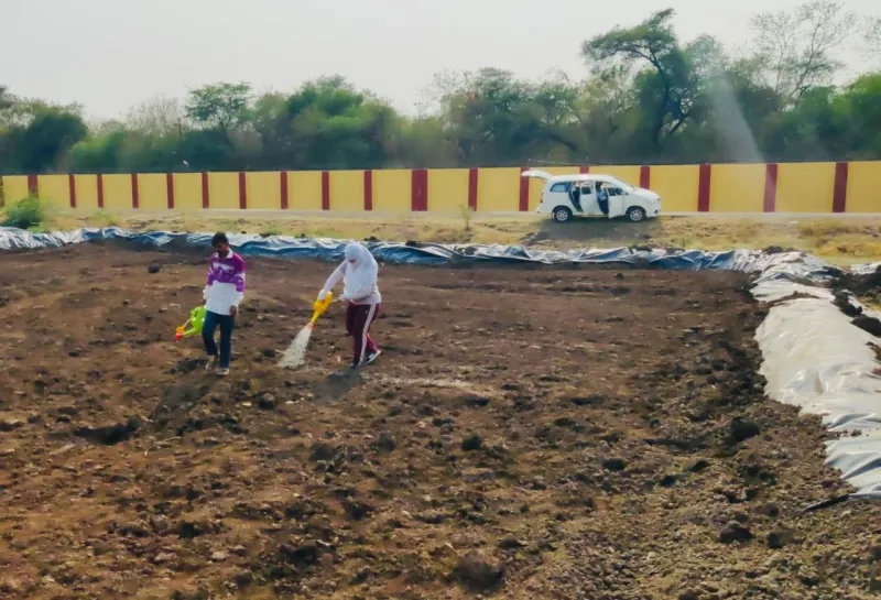 Two people working in the soil with a white van in the background.