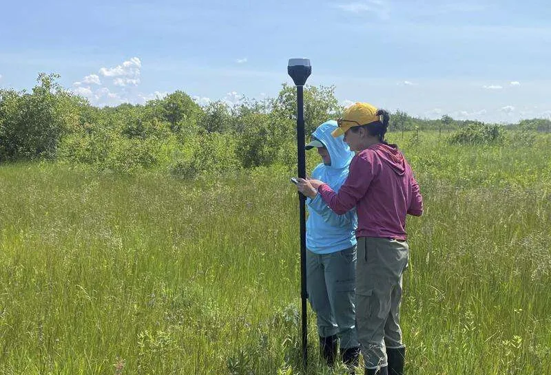 Josie Pickar standing in field holding research equipment with another scientist.