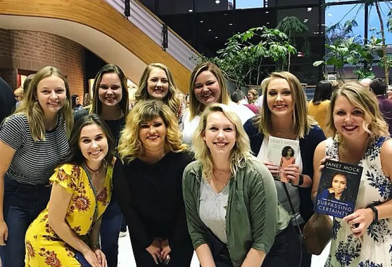 A group of women smiling confidently at the camera. Two of the women are holding books. 