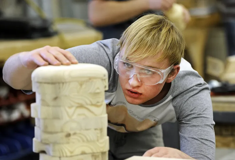 Student wearing protective eyeware while working on a wooden structure in woodshop.