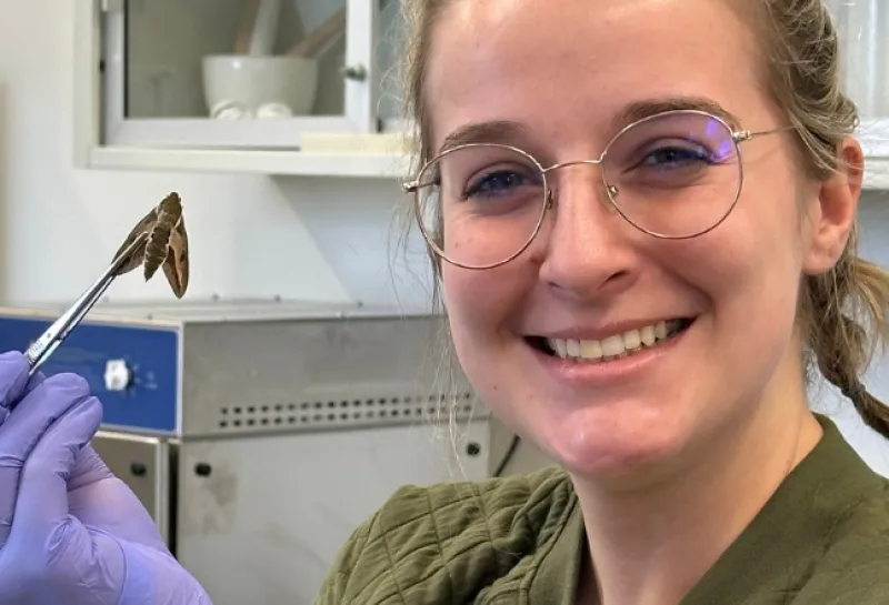 Trinity Atkins holding a moth with tweezers while smiling confidently at camera.