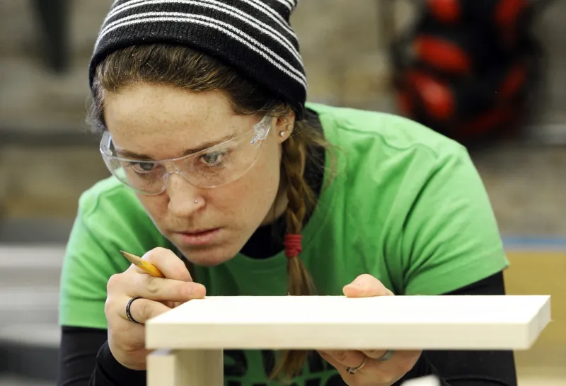Student wearing protective eyeware while working with wood in woodship.
