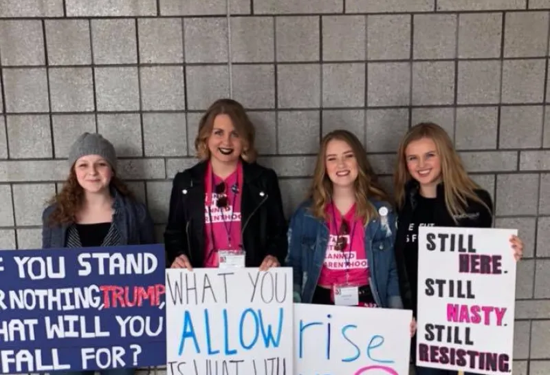 Women standing against concrete wall holding signs for the Women's March.