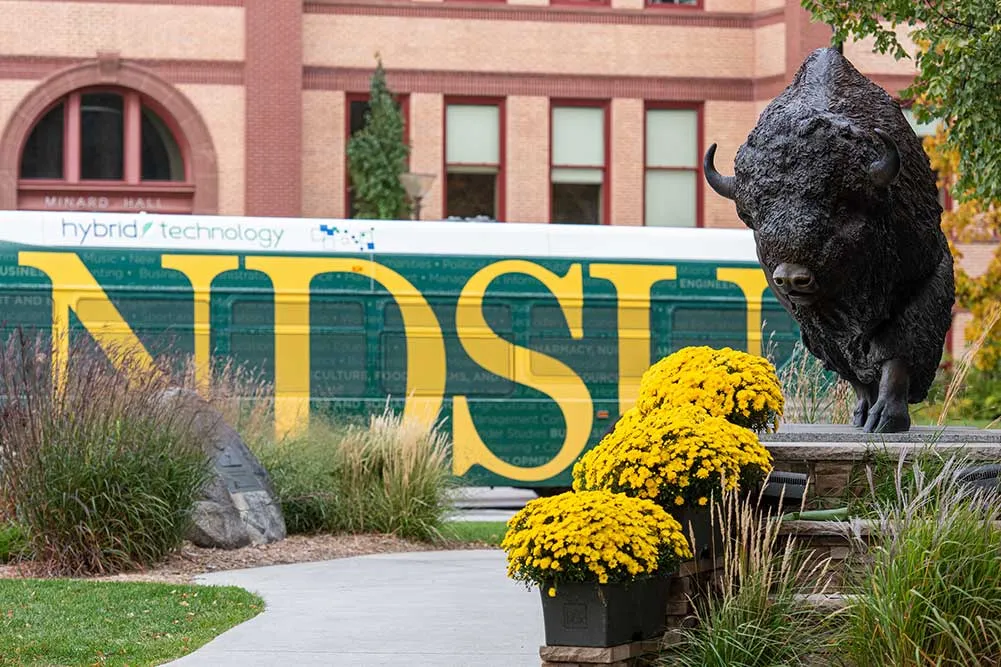Campus bus passes behind Bison statue.