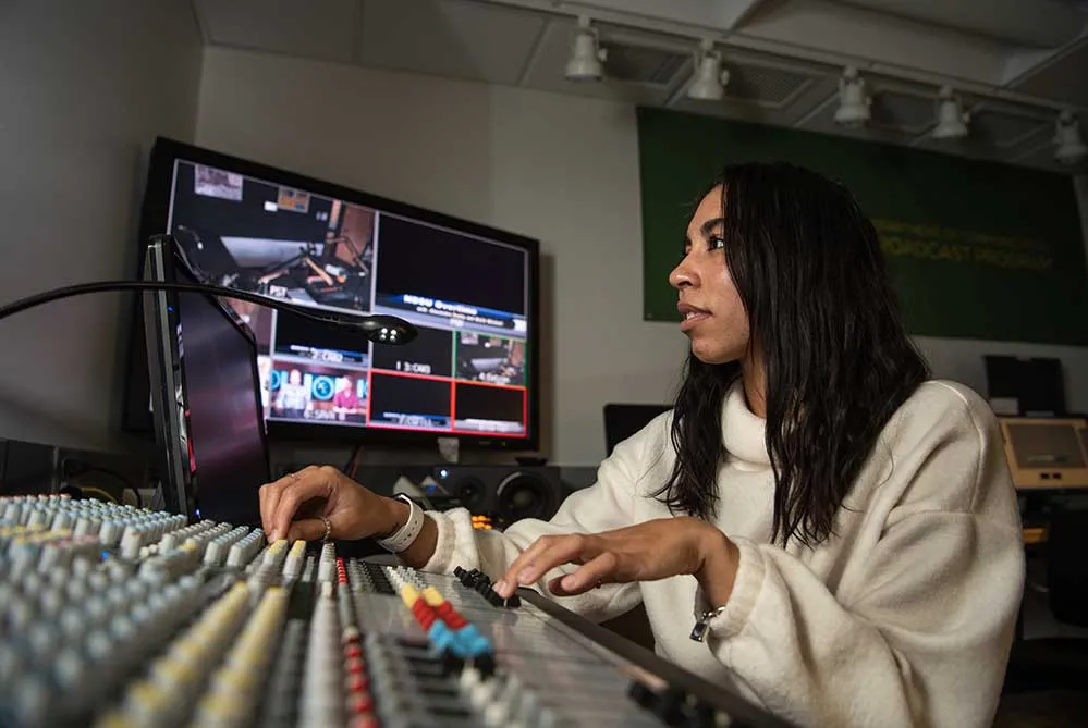student working at a mixing board in a recording booth