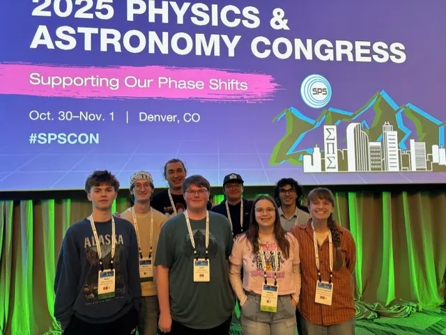 Several physics students behind a sign showing "2025 physics and astronomy congress"