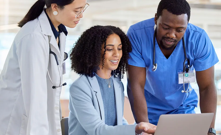 Three healthcare workers reviewing health records on a laptop