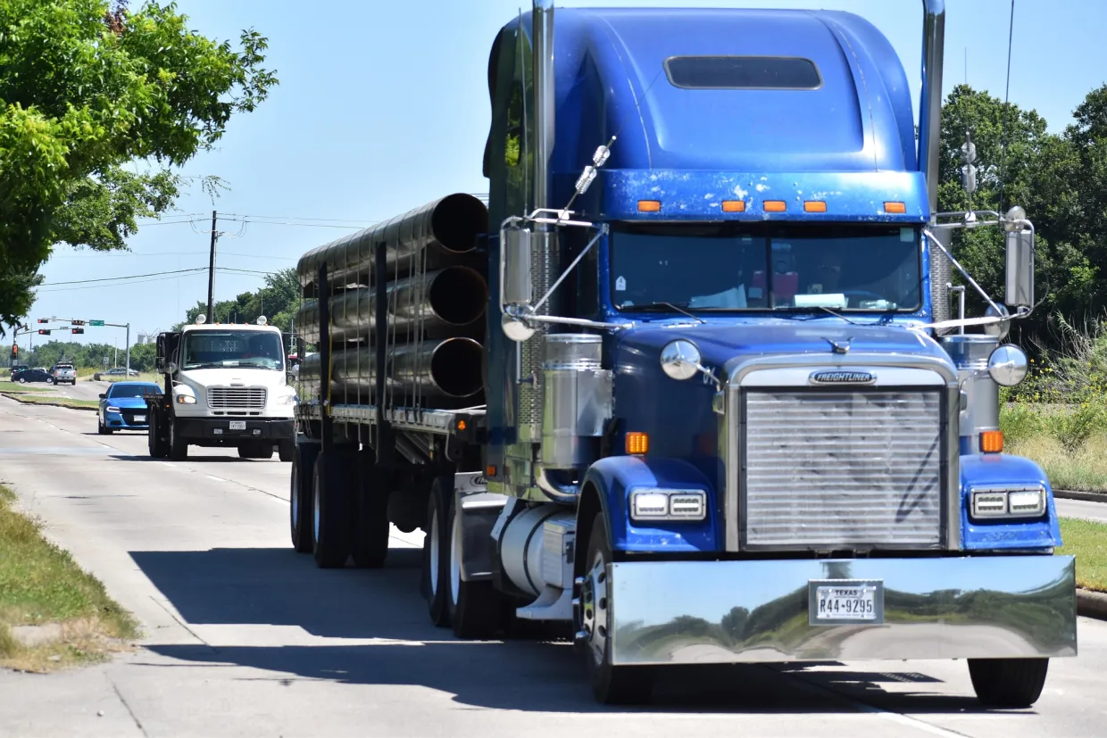Blue semi-truck carrying pipes coming down the road