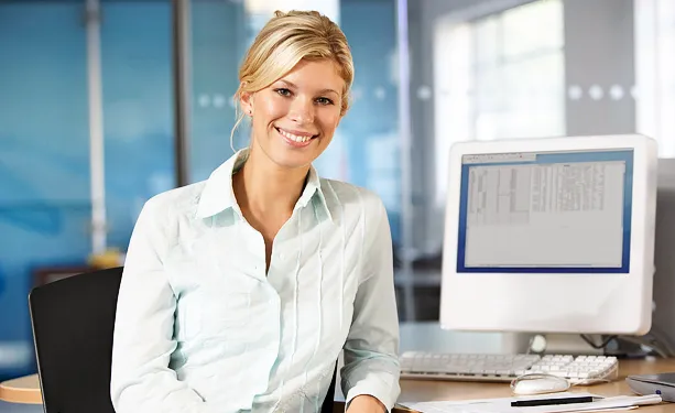 Woman smiling at an office with monitor and keyboard in the background