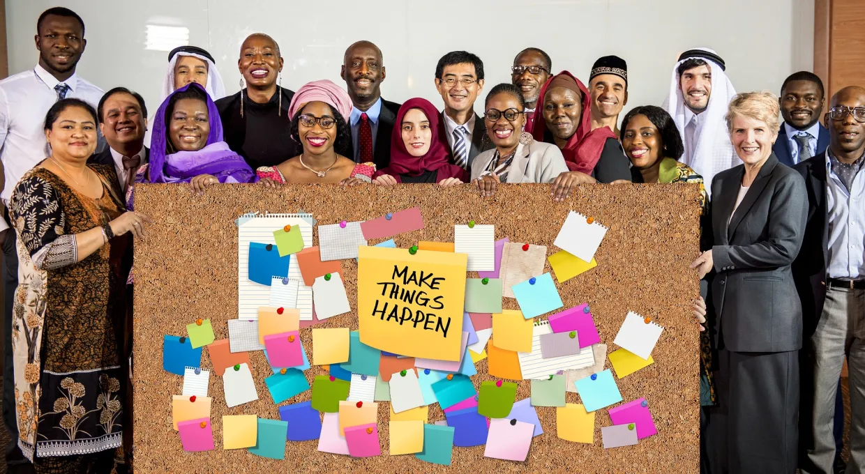 Global Business Leaders standing behind a bulletin board with post notes and a sign that says Make things Happen