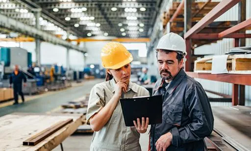 Two employees looking at a clipboard in a manufacturing plant