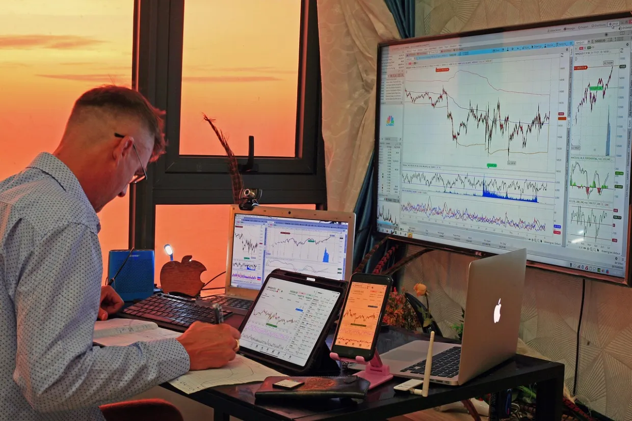 man at a desk looking at stock trading reports on three different displays