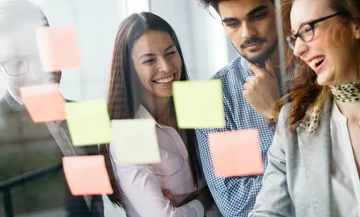 Four project managers laughing while working on a project looking at post-it notes on window
