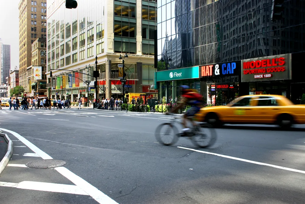 city street with buildings on right, a taxi, and cyclist on the road