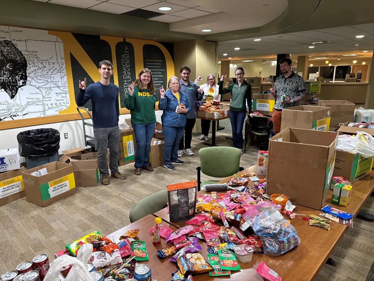 A group of people stand in from of tables full of food items.